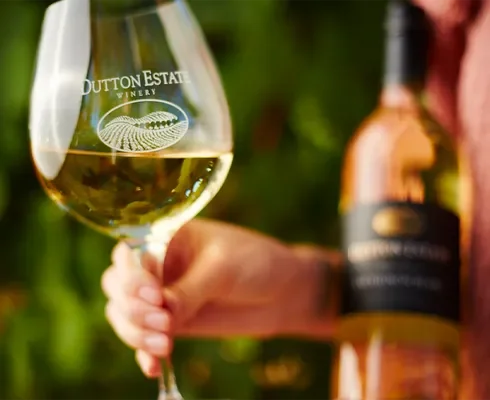 A person holding a glass of white wine with a winery logo that reads 'Button Estate Winery.'