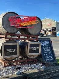 Sign for Rocket City Roadhouse with two large black pipes on a red truck, outdoor scene with a building in the background and a blue sky.