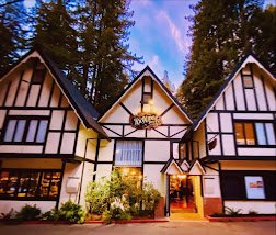 A Tudor-style resort lodge with exposed wooden beams, white stucco walls, and a gabled roof, set against a backdrop of tall pine trees.