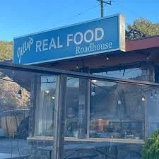 Signboard reading 'Real Food Roadhouse' outside a restaurant with glass windows.