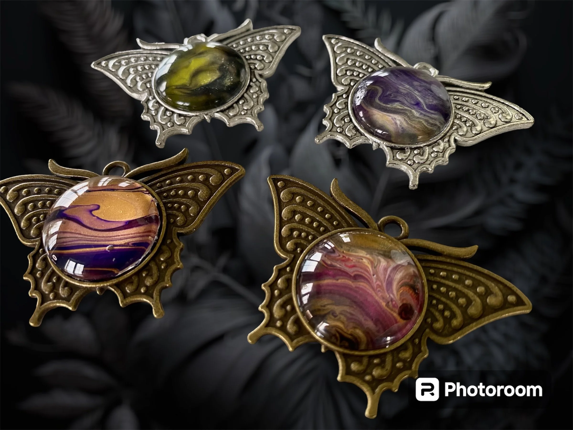 Close-up of vintage style butterfly brooches with gold-tone metal wings and large colorful glass cabochon bodies, set against dark background.