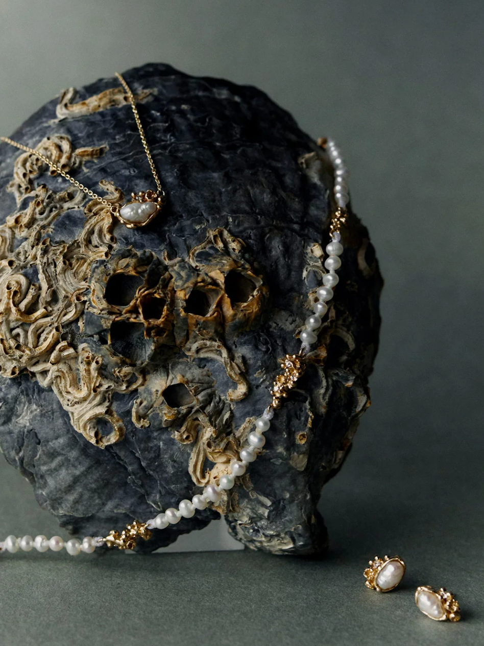 Pearl jewelry, including a necklace and earrings, displayed on a dark, textured rock with barnacle-like formations.