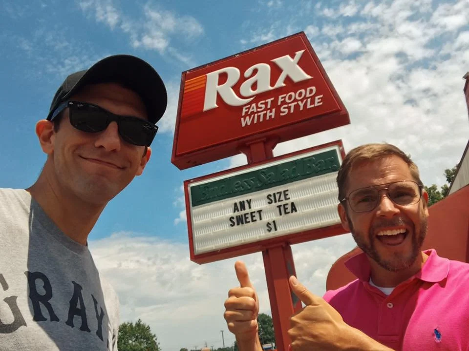 Director Chris Preksta and star Curt Wootton standing in front of the sign for Rax restaurant.
