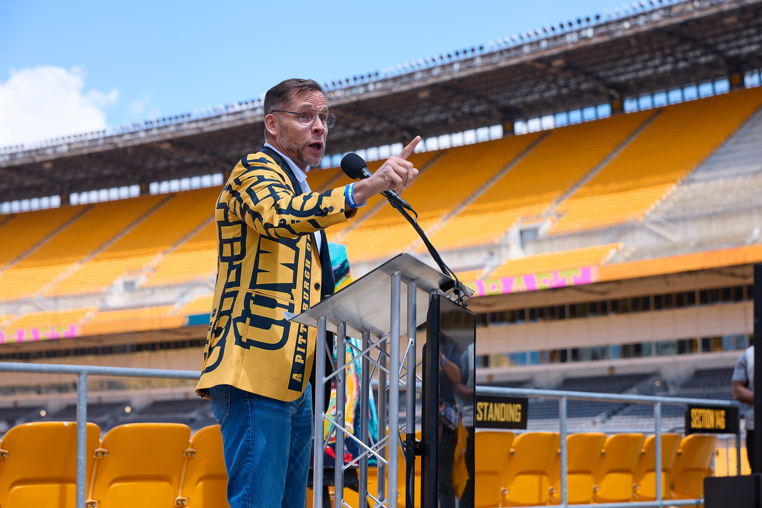Pittsburgh Dad in a Terrible Towel themed suit jacket speaking at an event at Acrisure Stadium during the NFL Draft.