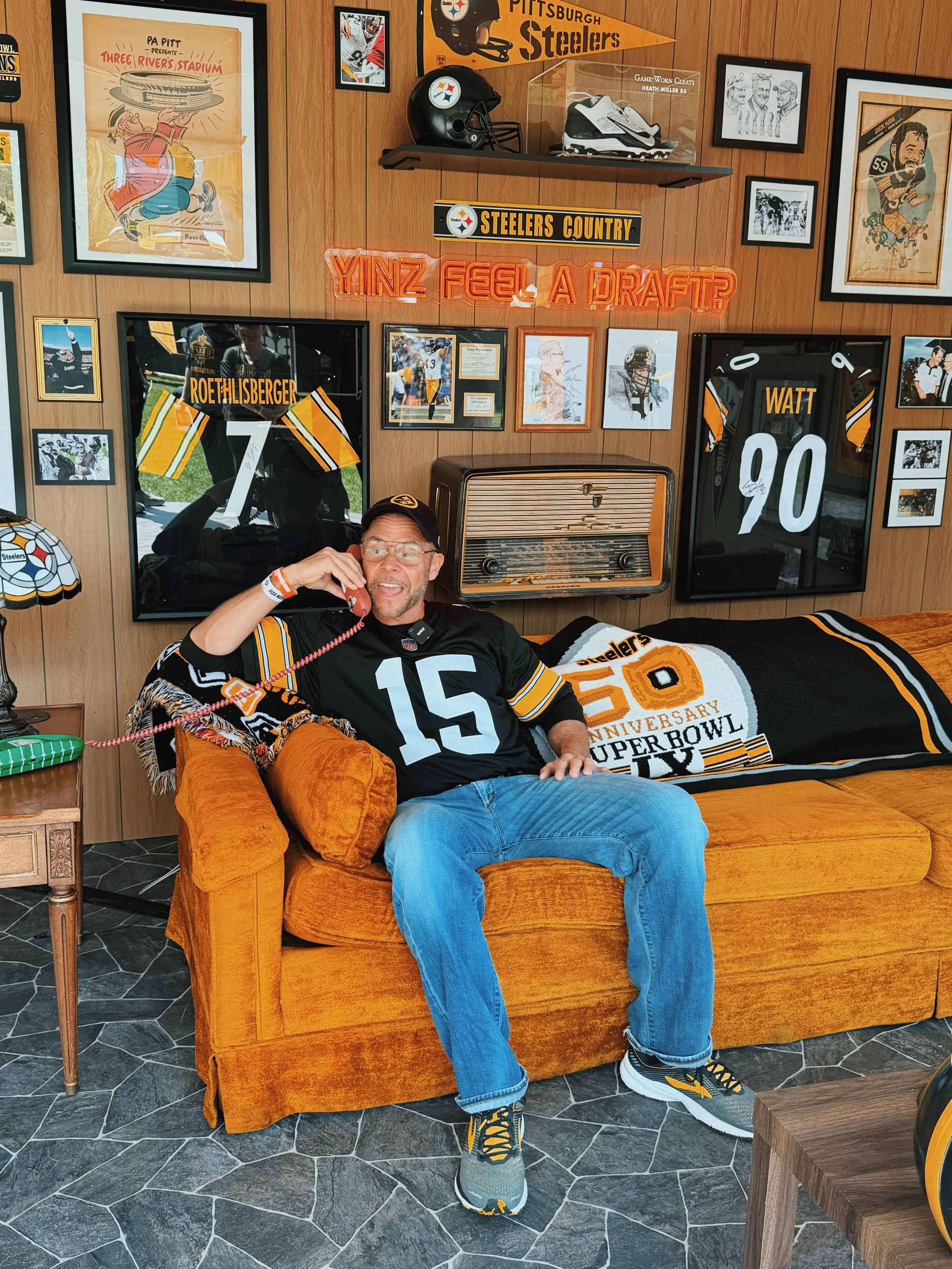 Pittsburgh Dad sitting on a couch in a 1970s themed basement covered with Steelers memorabilia.
