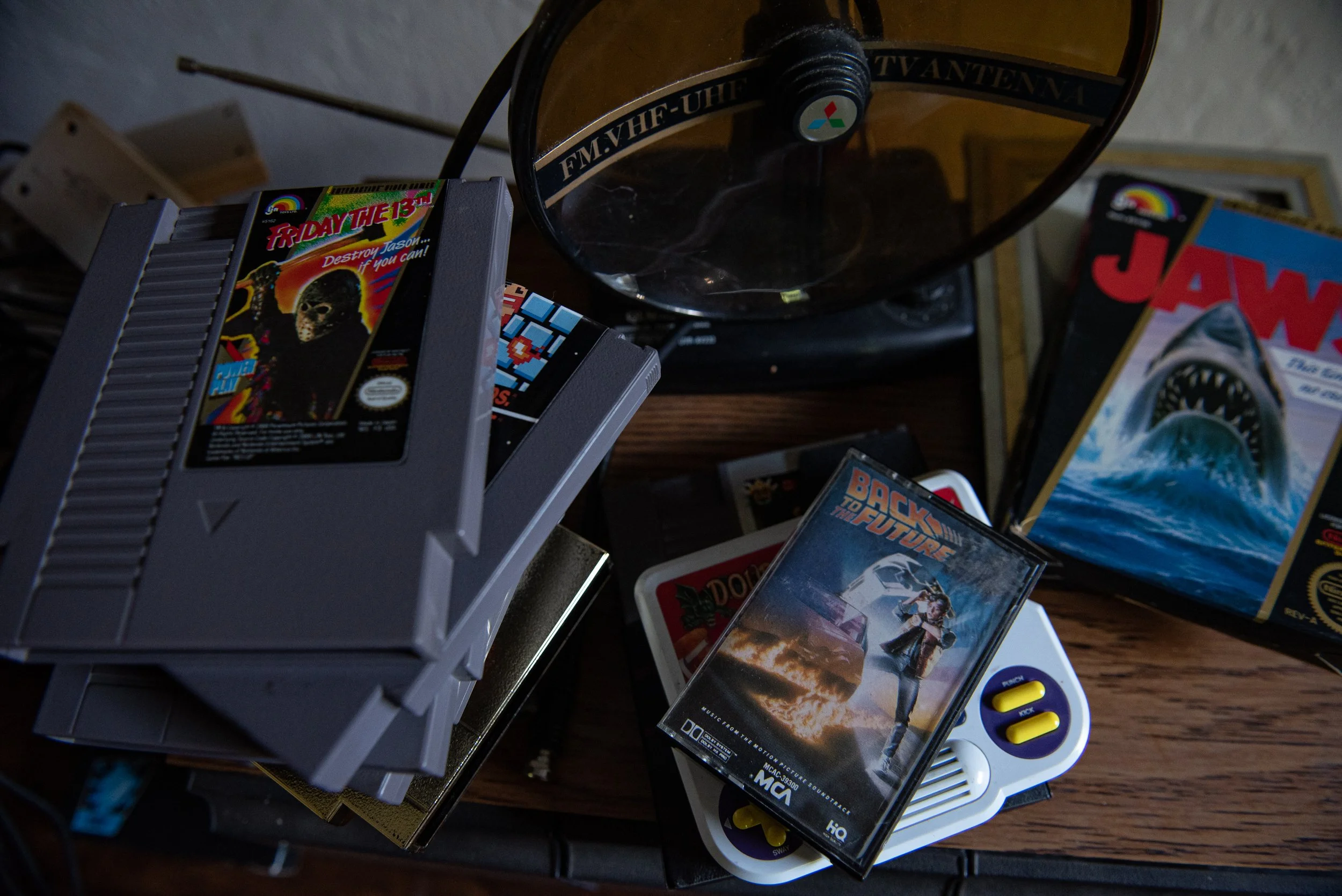 Photo of vintage video game cartridges and a small white electronic device with yellow and purple buttons, along with a black object with a clear plastic dome and some other gaming-related items on a wooden surface.