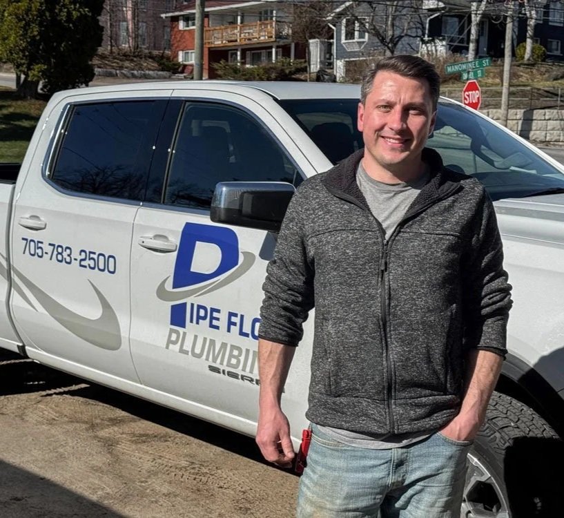 Jordan from Pipe Flow Plumbing standing outside next to his white pickup truck with the Pipe Flow Plumbing company logo and contact information on the side of the truck.