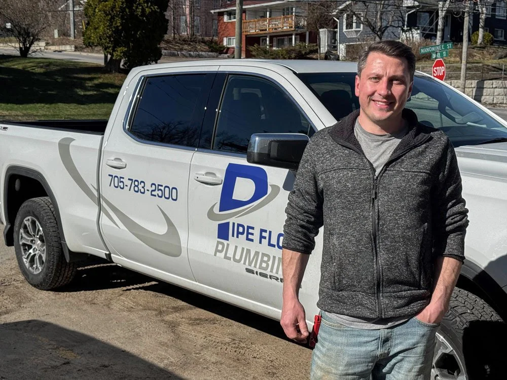 Pipe Flow Plumbing's Jordan standing in front of his white pickup truck that has Pipe Flow Plumbing lettering and graphics, including a phone number.  He has a pleasant smile and is welcoming.