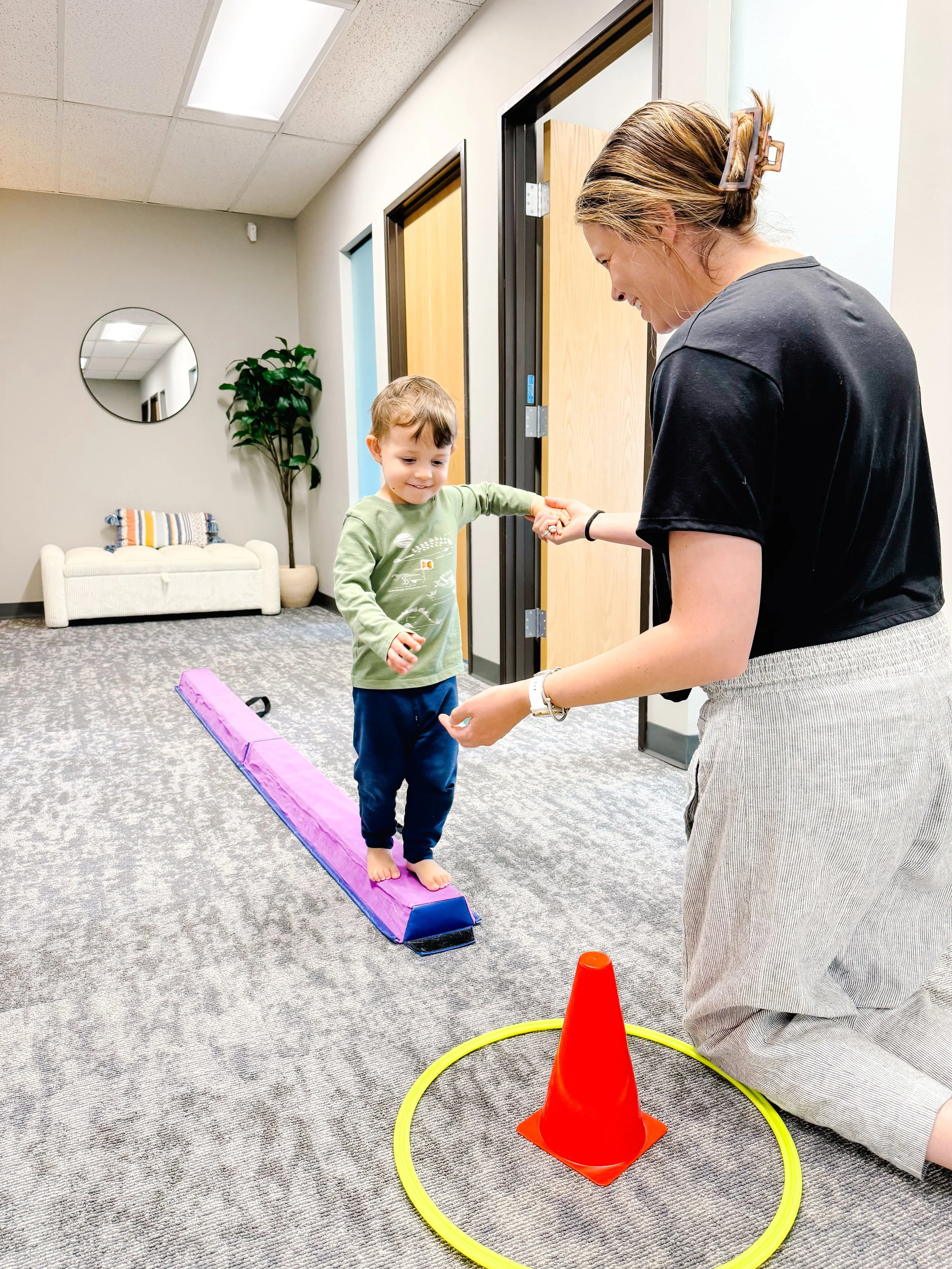 child getting help from therapist on balance beam