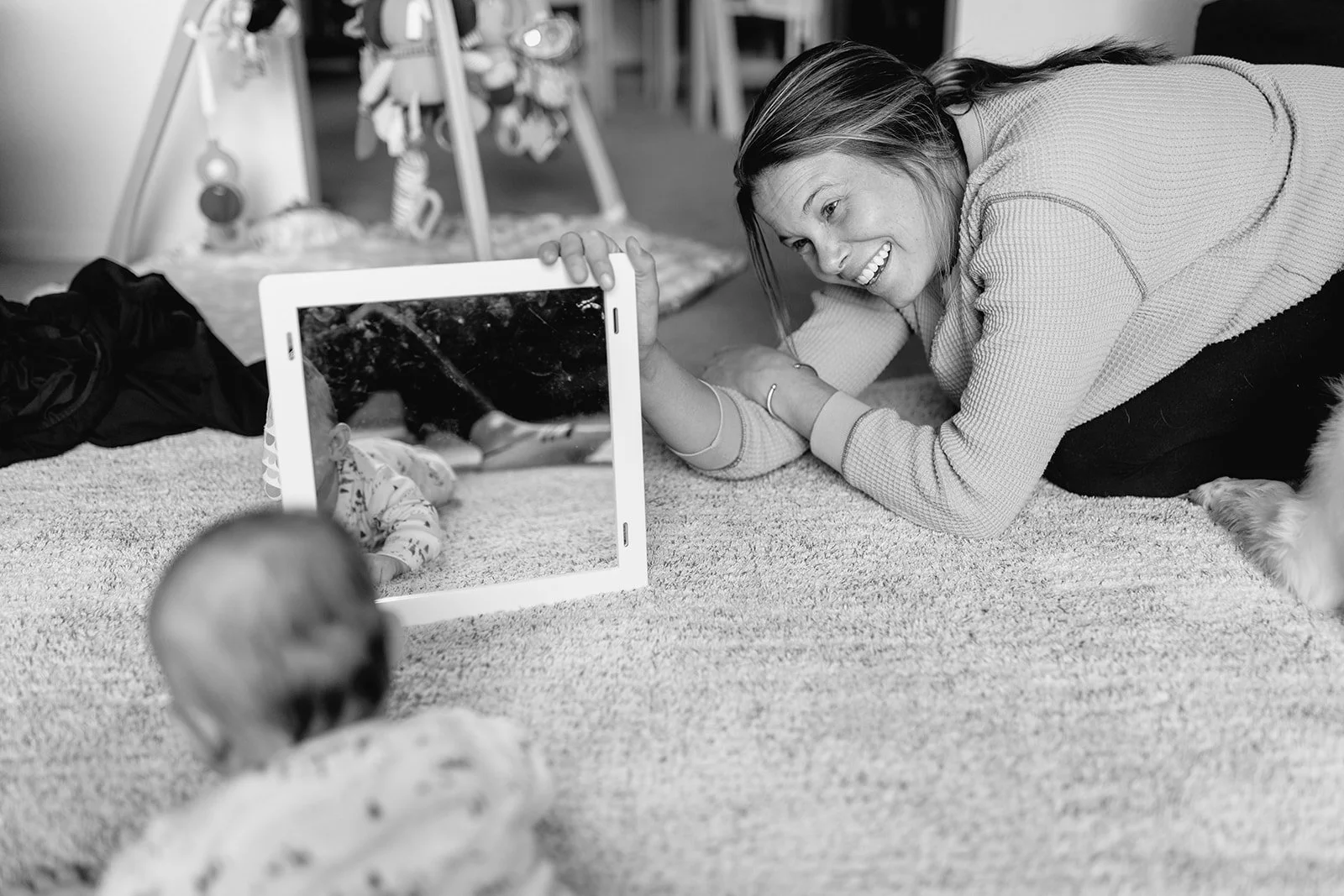 baby in tummy time looking at a mirror and mom smiling  back