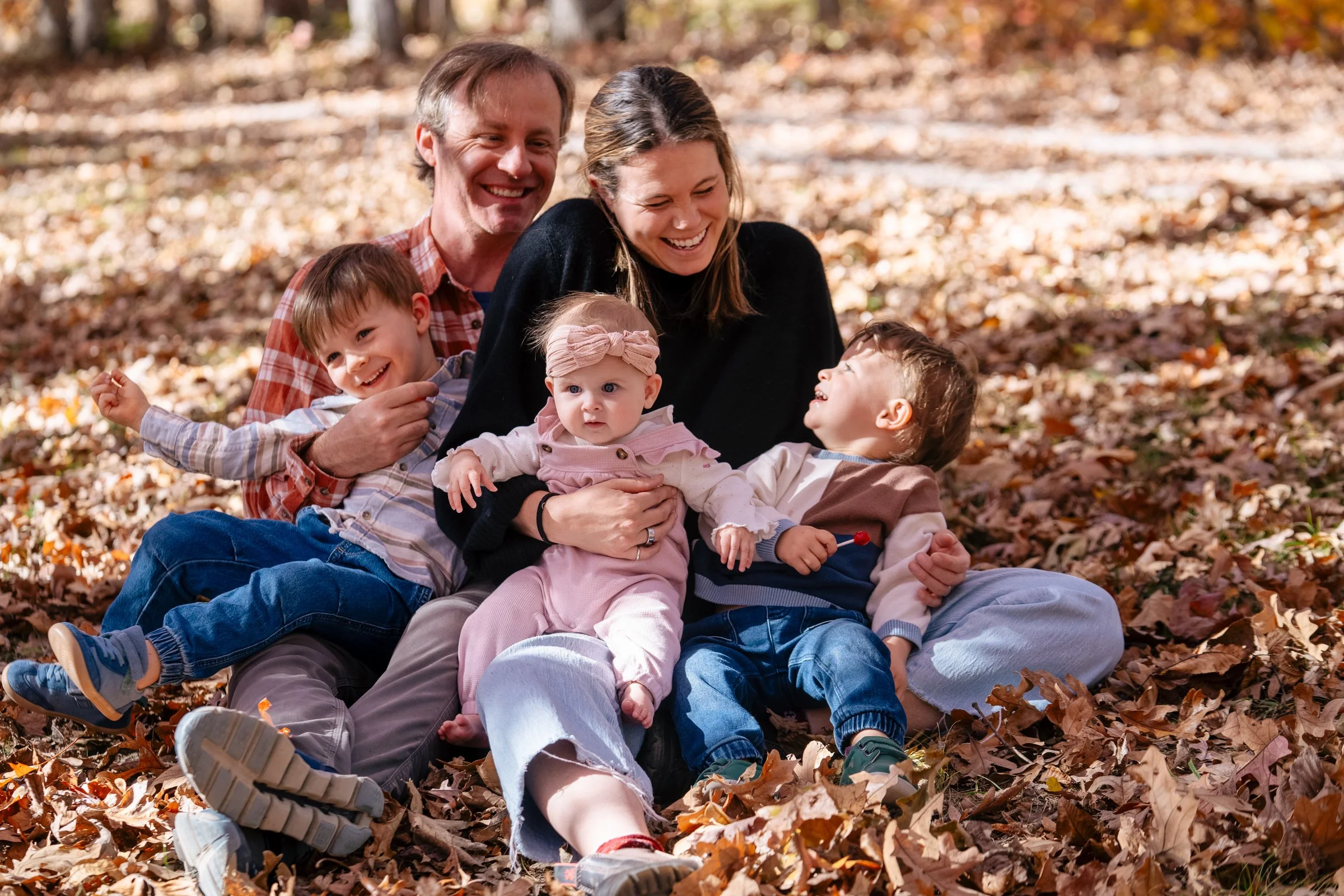 mom, dad, three kids, sitting in leaves laughing and smiling