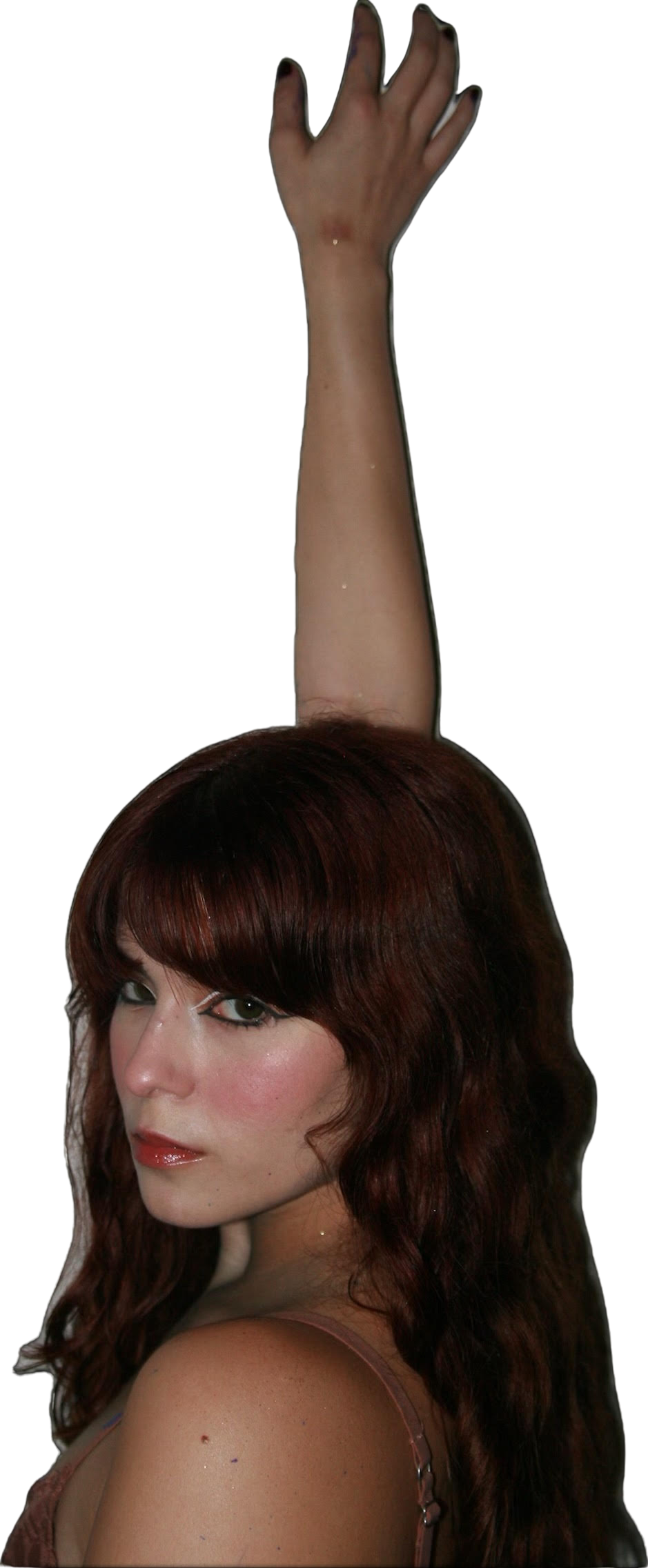 A woman with long, wavy brown hair and green eyes looking over her shoulder, wearing a nude-colored top.