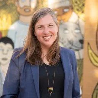 A woman in a suit standing in front of a colorful mural