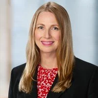 Headshot of smiling woman in a dark blazer and a red shirt. The woman has light skin and blonde hair.