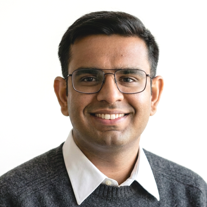 A young man with short dark hair, glasses, and a friendly smile, wearing a white shirt and dark sweater, against a plain white background.