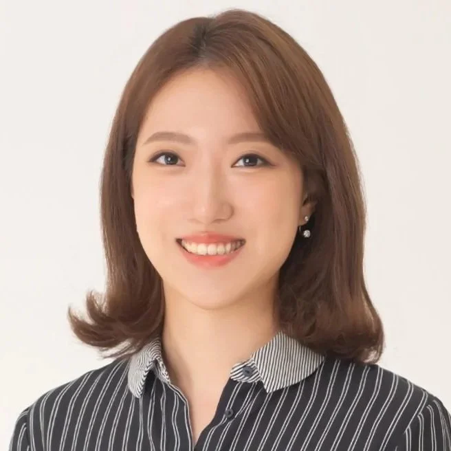A woman with shoulder-length brown hair, wearing a black and white striped shirt and pearl earrings, smiling against a white background.