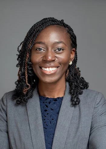 Portrait of a woman with braided hair in a gray blazer smiling at the camera.