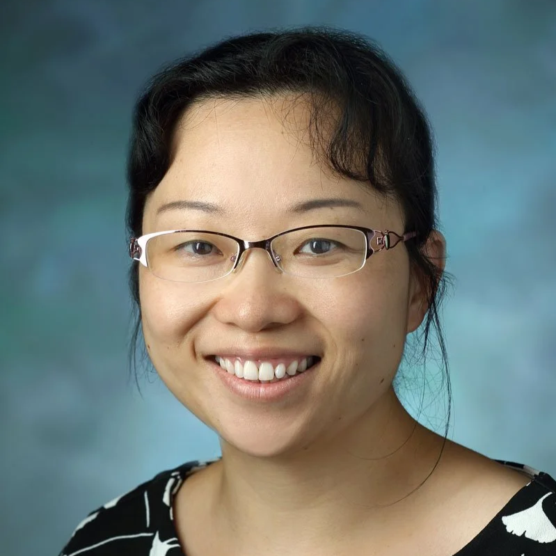 Portrait of a smiling woman wearing glasses with a dark and abstract background.