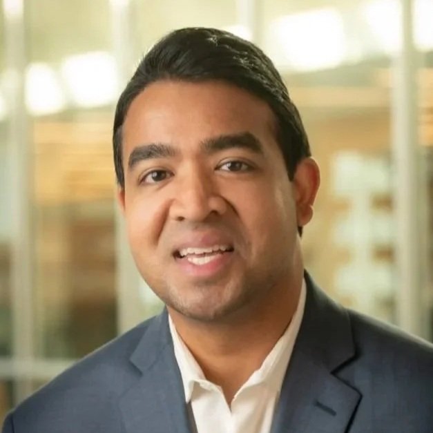 Professional portrait of a man in a suit with a blurred office background.