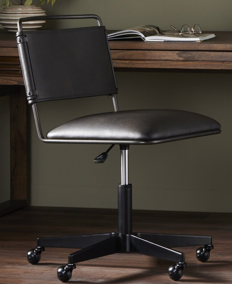 Black office chair with a cushioned seat and backrest, on wheels, in front of a wooden desk with books and glasses on top.
