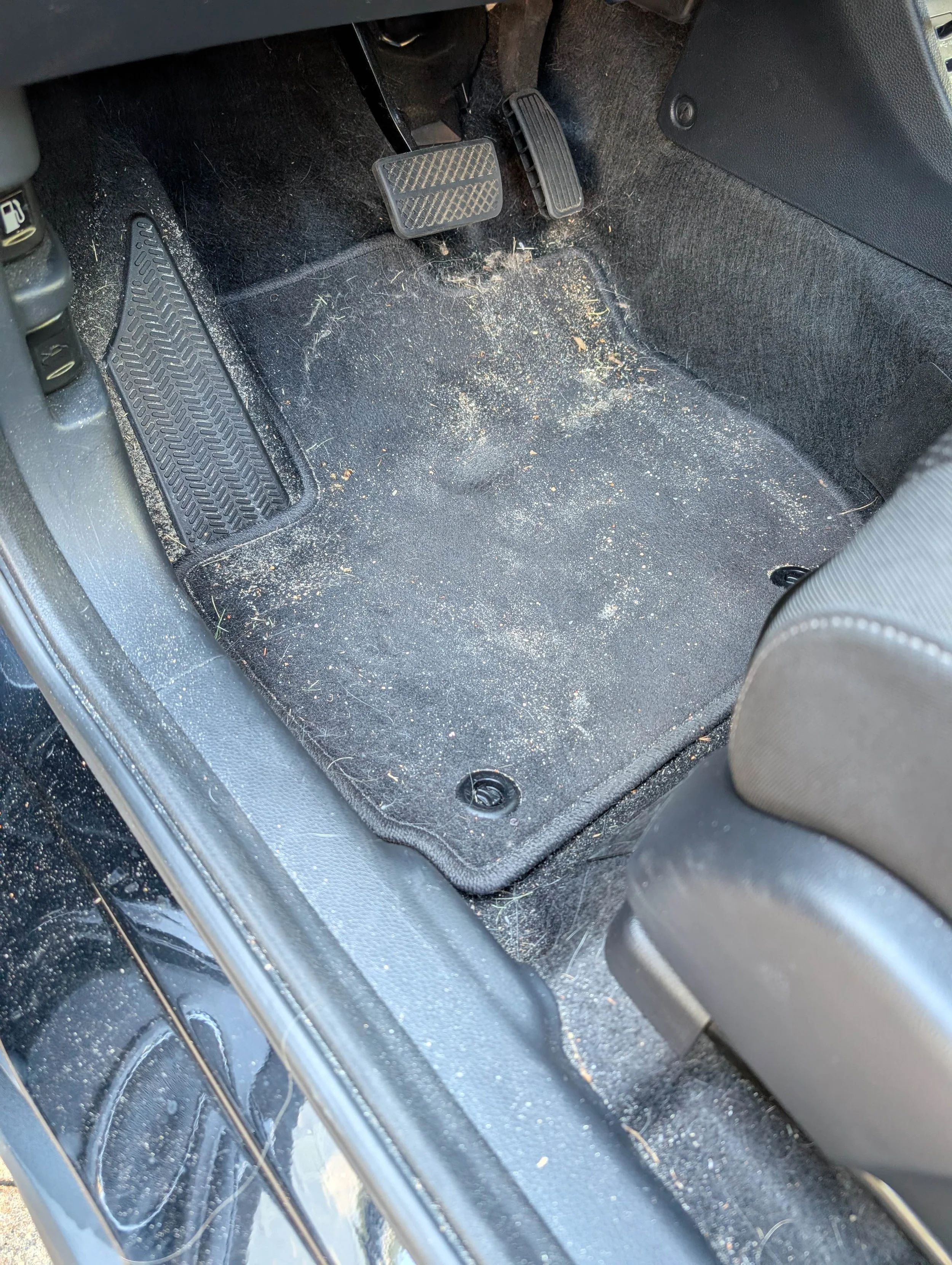 Dirty car floor with dirt, crumbs, and debris around the brake and accelerator pedals.