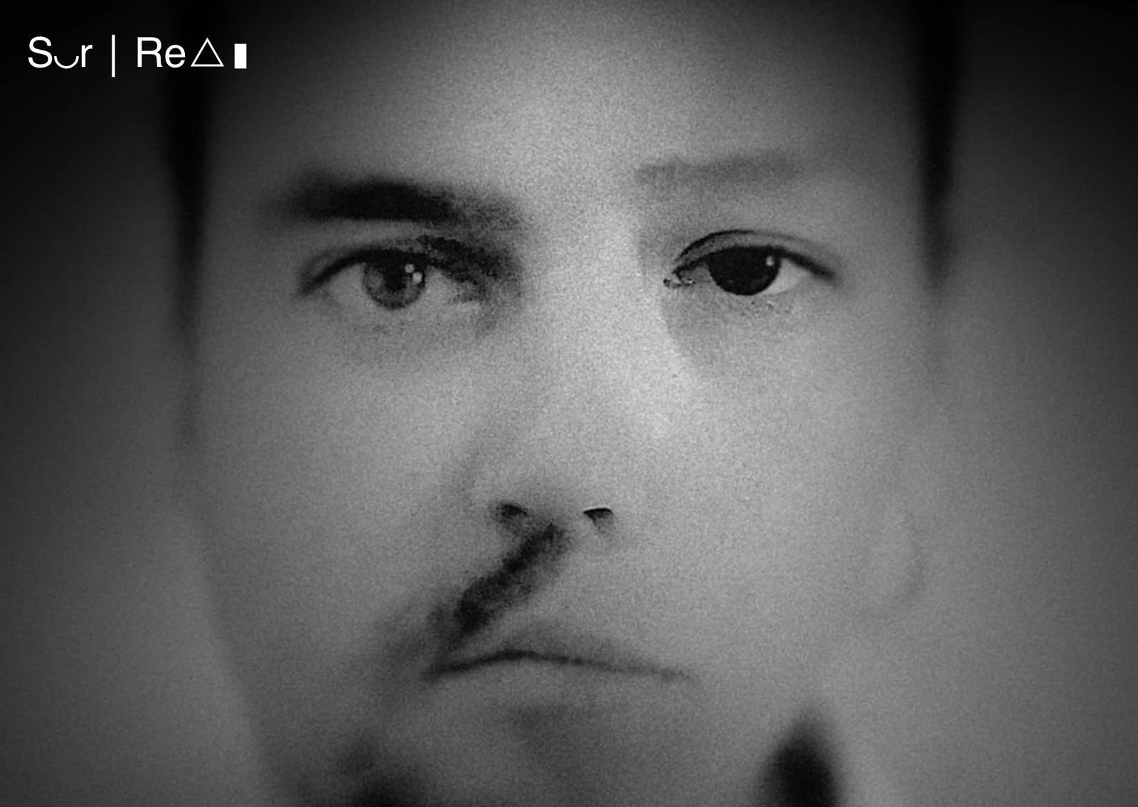 Black and white close-up of a person's face with a serious expression, slightly obscured and fuzzy, with text overlay in the upper left corner.