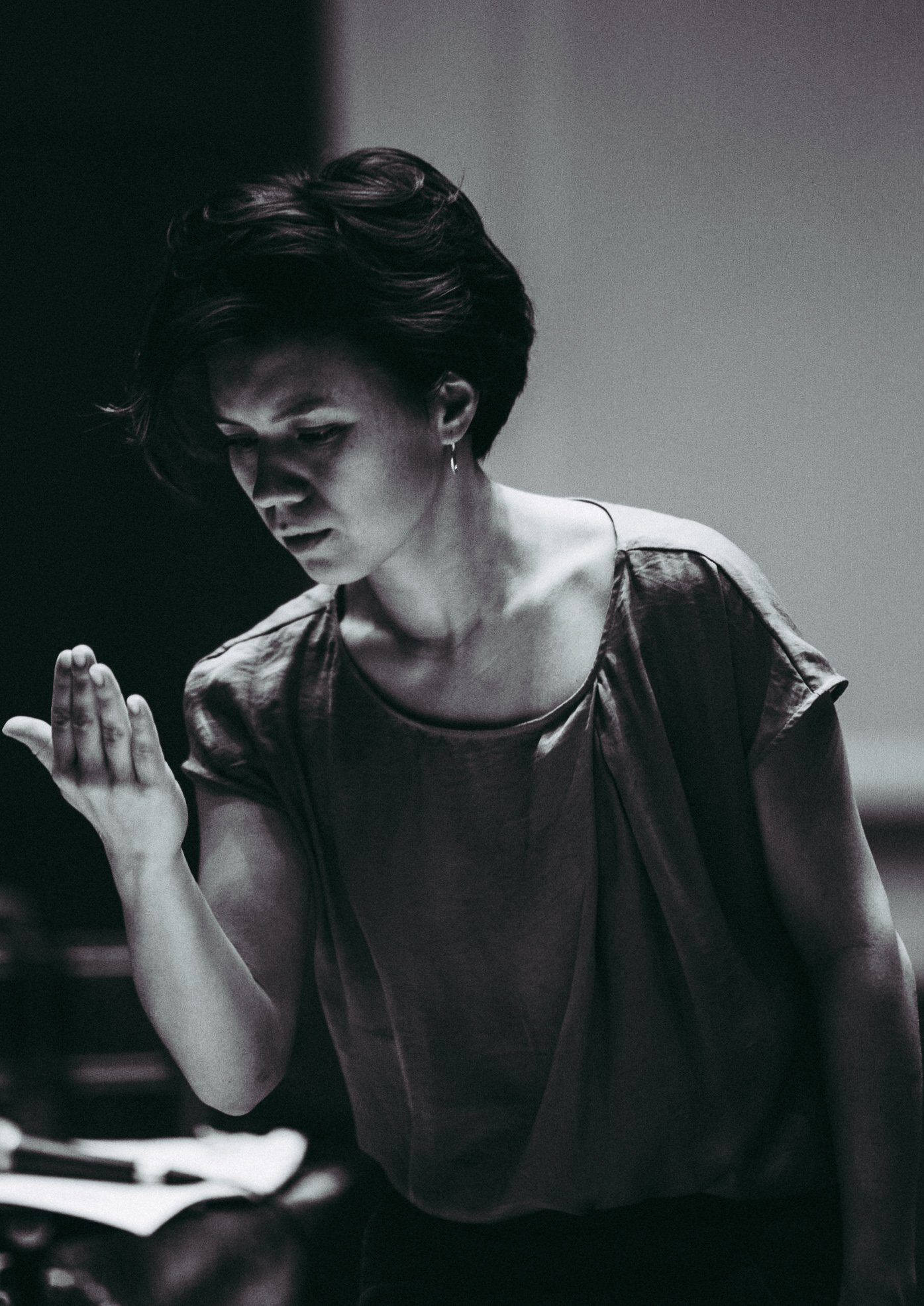 A black and white photo of a woman looking down and holding her hand up in front of her face, appearing focused or contemplative.