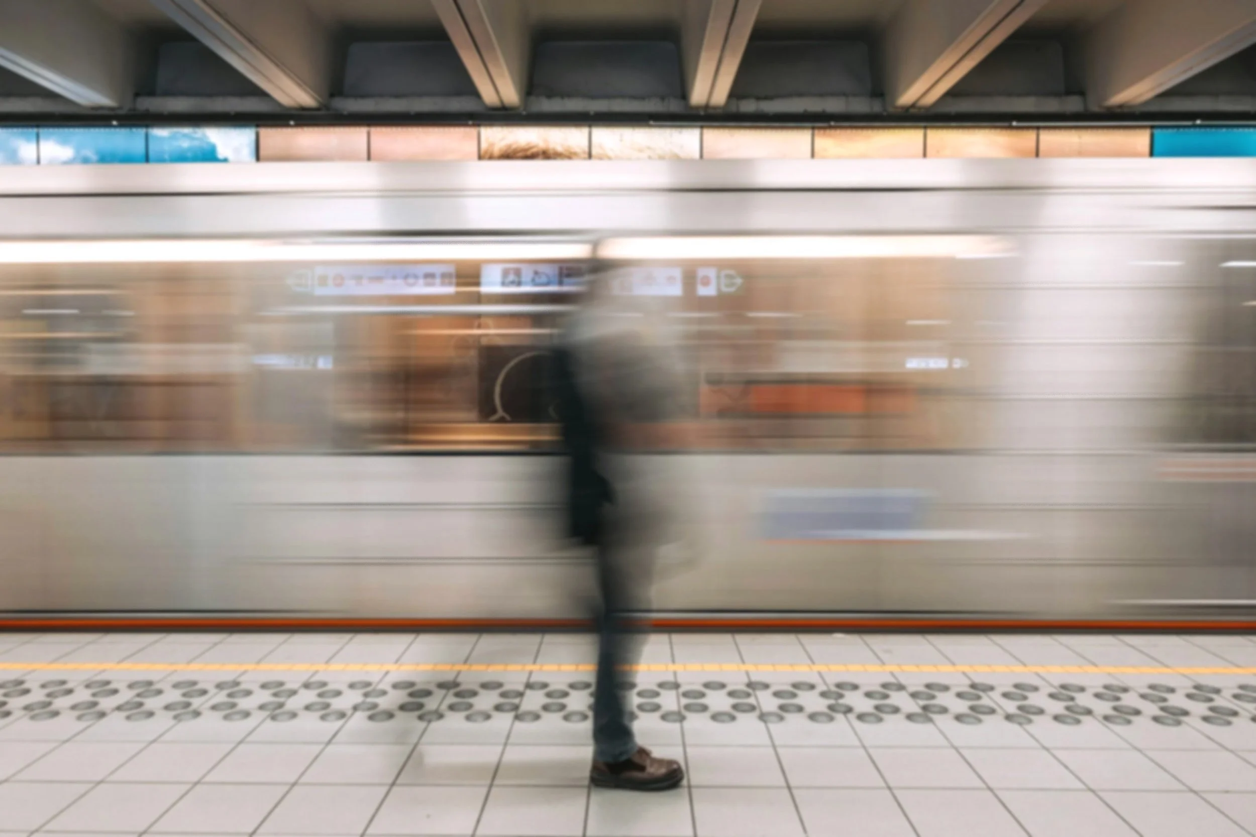 Person standing on a train platform next to a moving train, with their face not visible.
