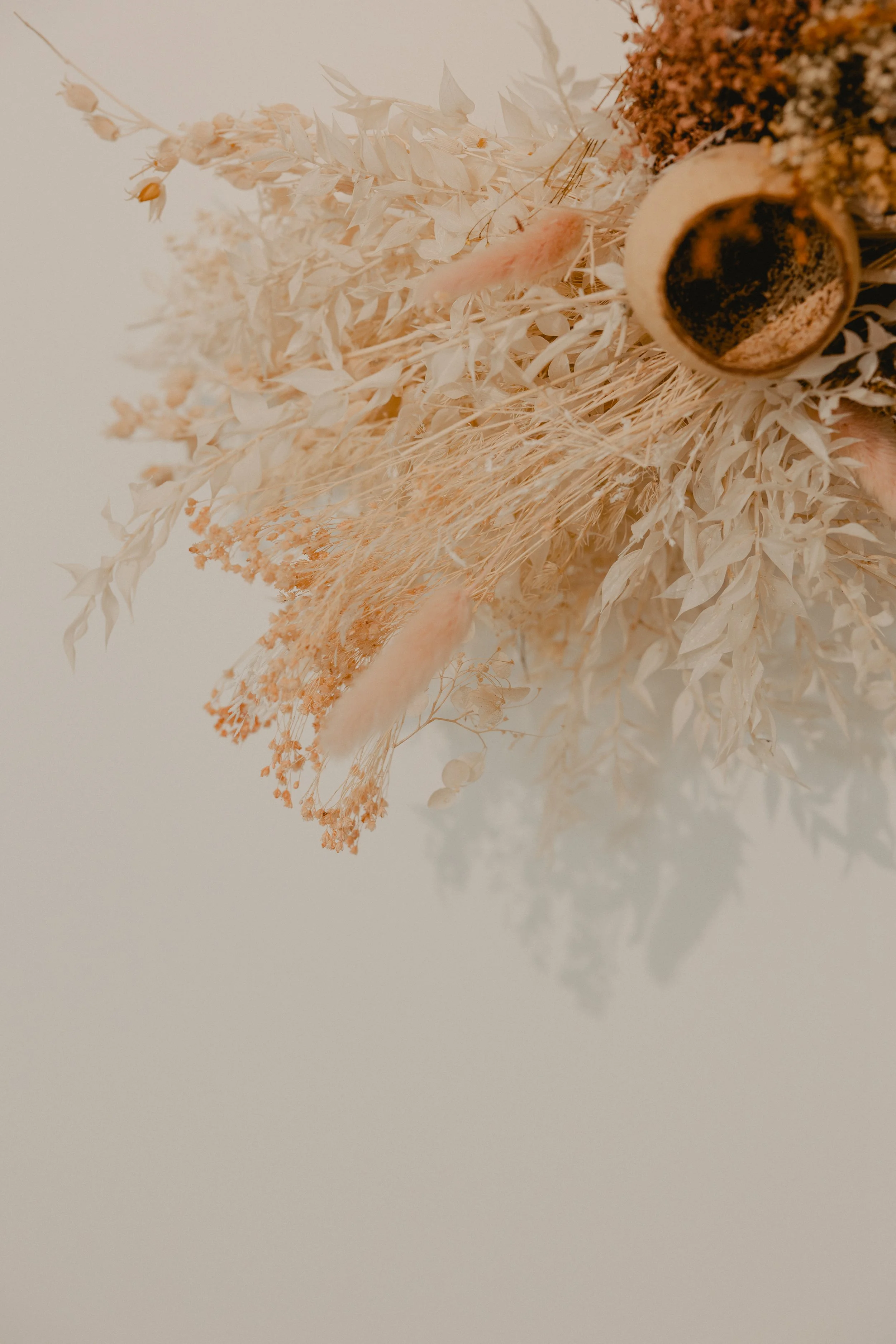 A floral arrangement with dried white and pinkish flowers and a small cup of coffee on a white background.