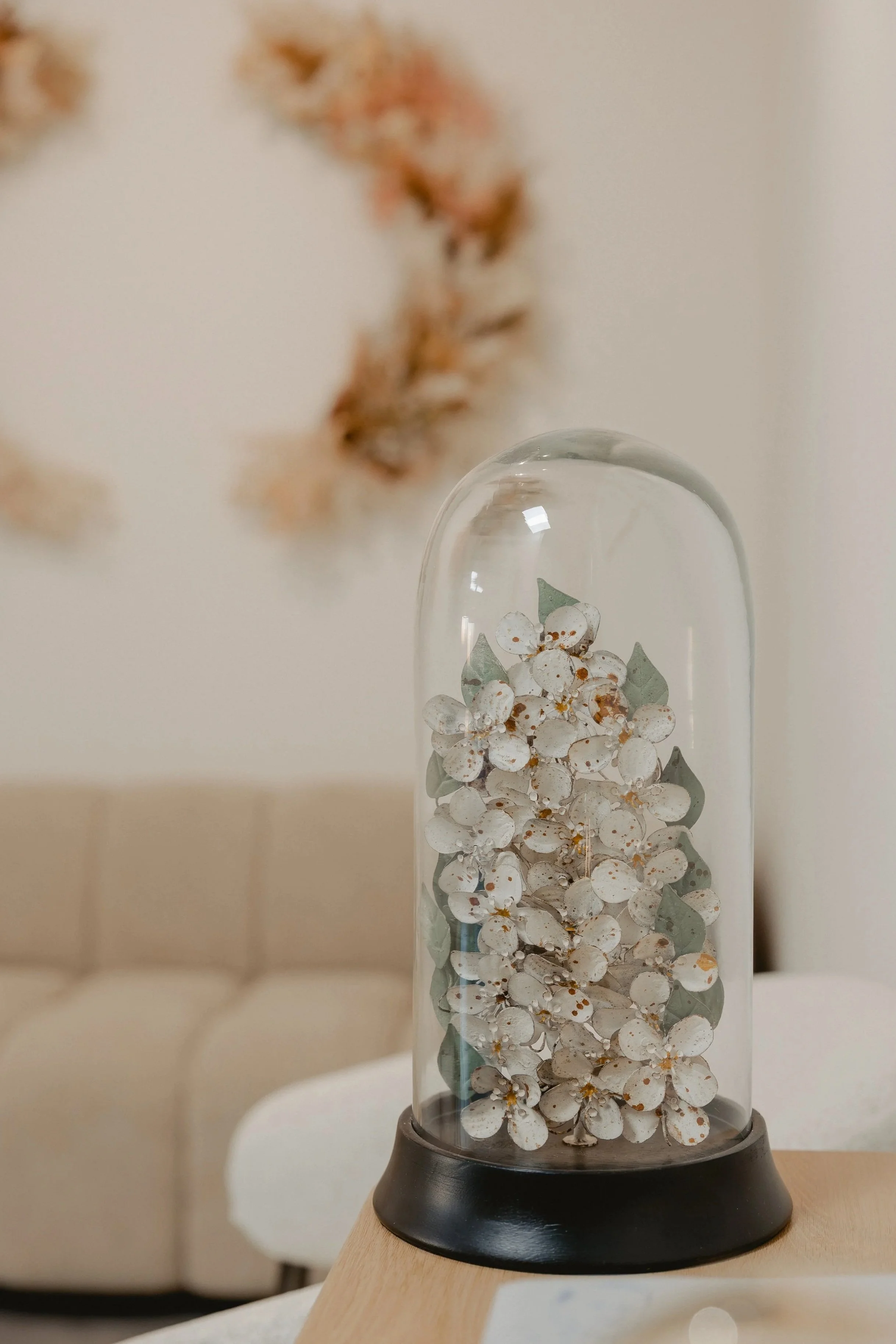 A glass dome containing white flowers with brown spots on a white surface.