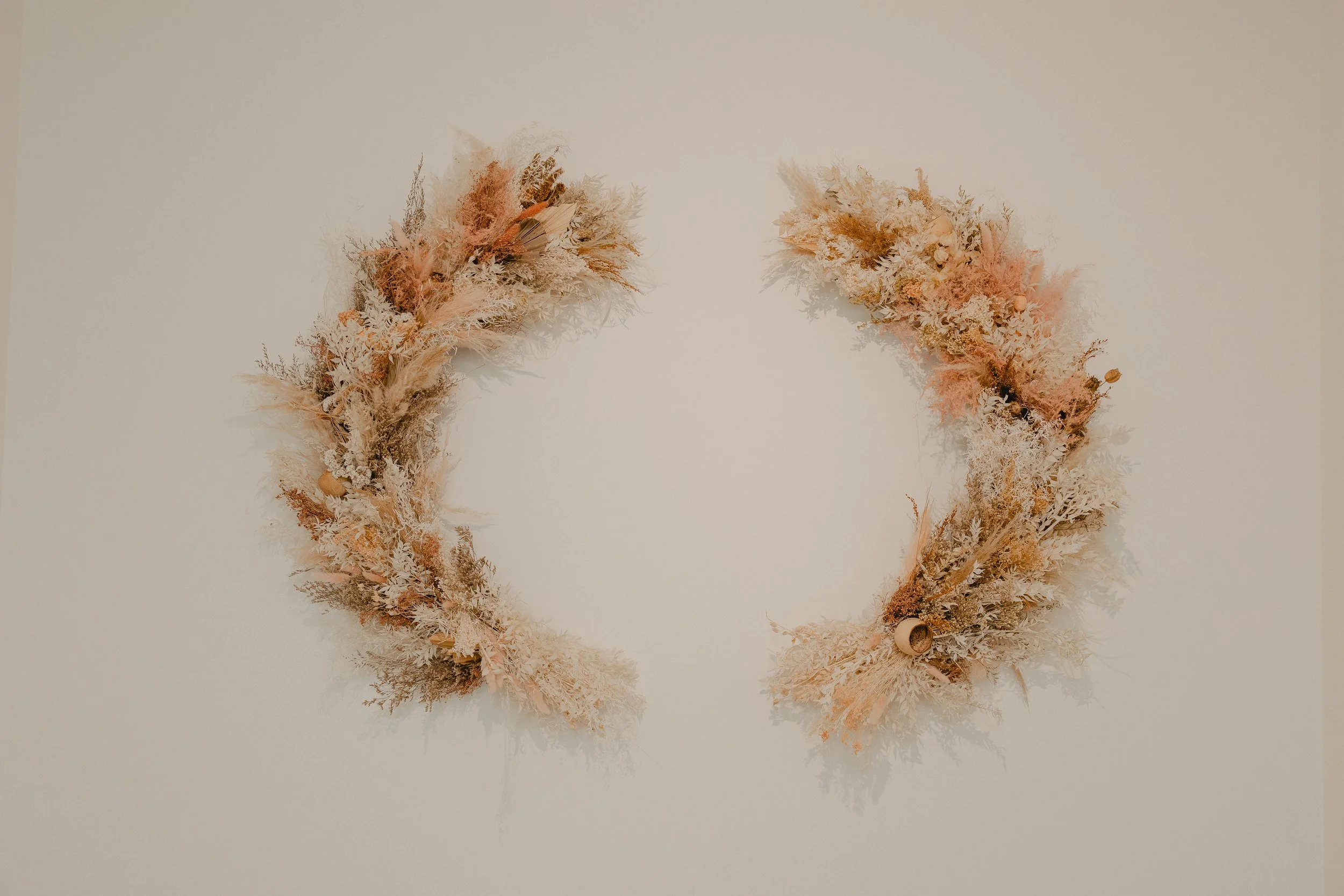 Two dried floral arrangements in soft pastel shades, positioned symmetrically on a plain, light-colored background.