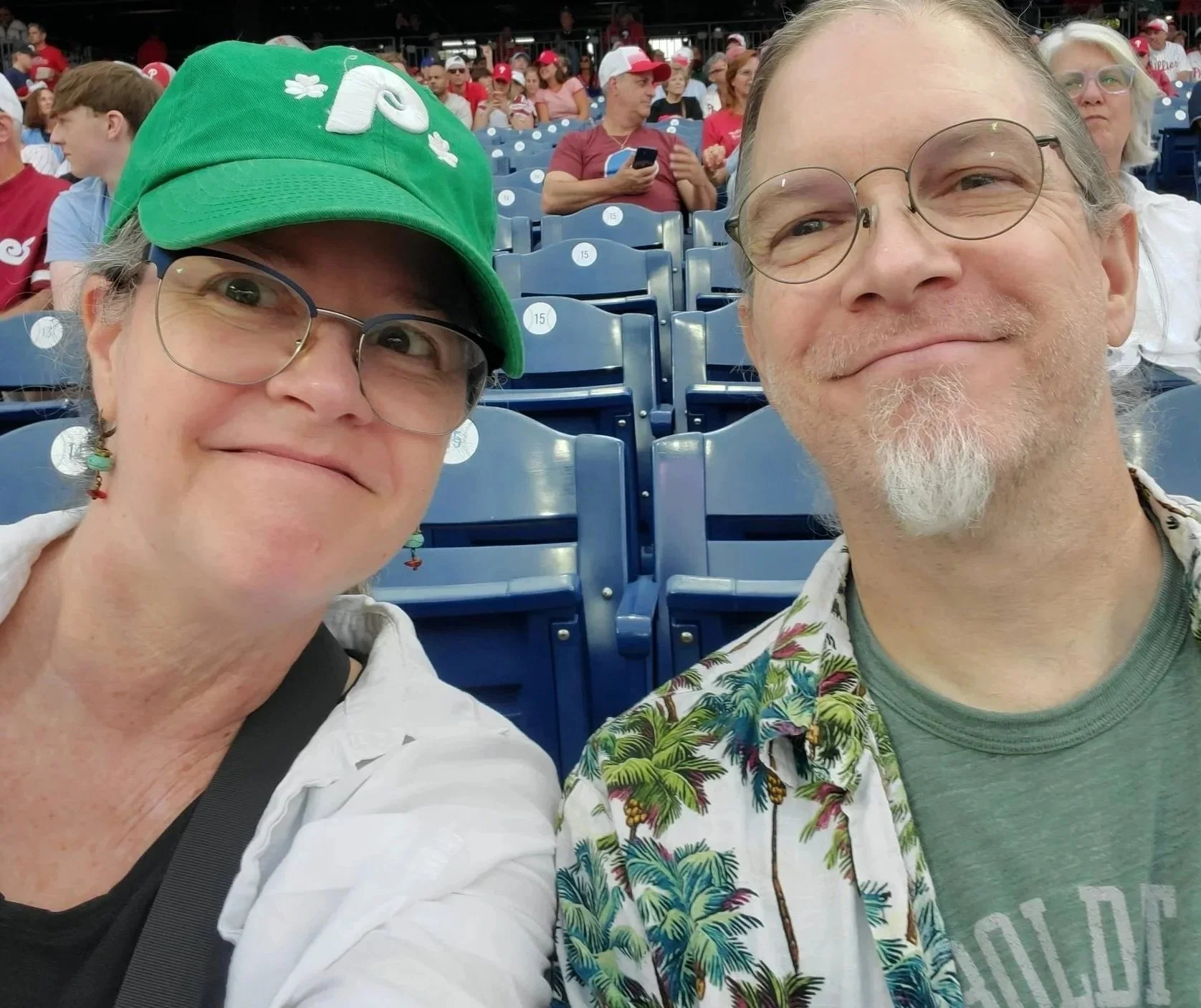 Kerry wearing a green Phillies baseball cap and husband are seated in the stands.