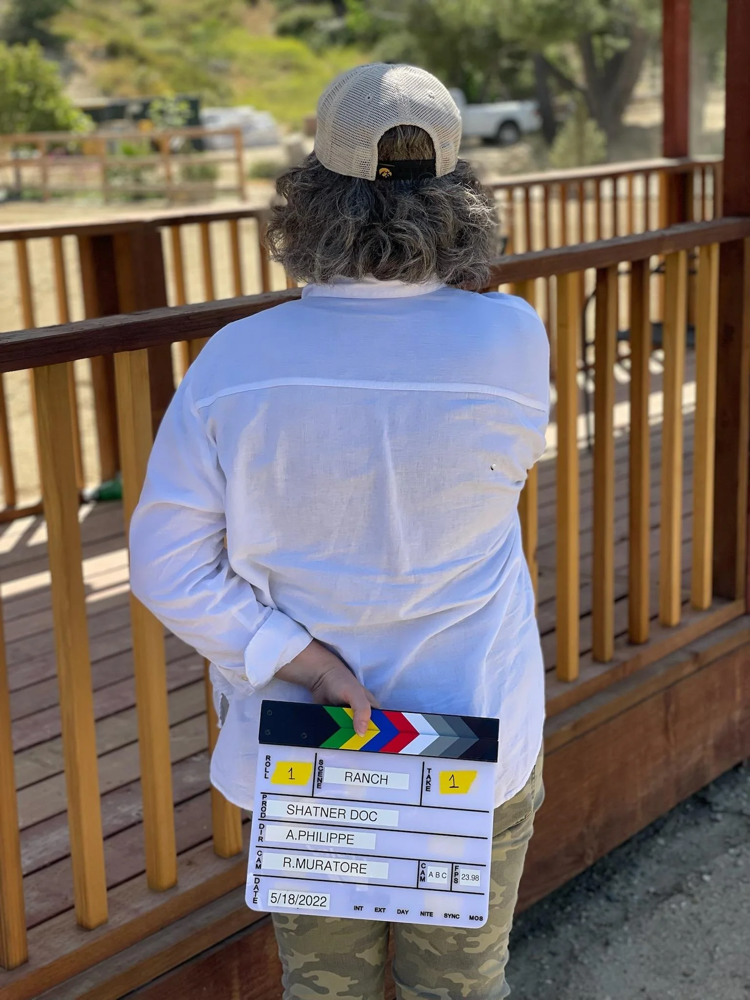 A photo taken from behind Kerry who is holding a slate behind her back watching filming in the distance.
