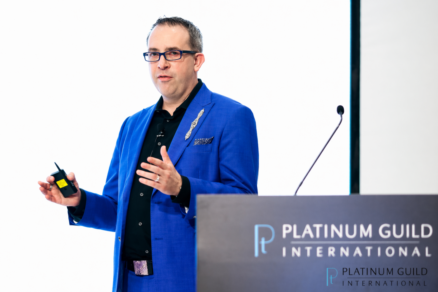 Man giving a presentation at a conference, standing behind a podium with the logo and name 'Platinum Guild International'.