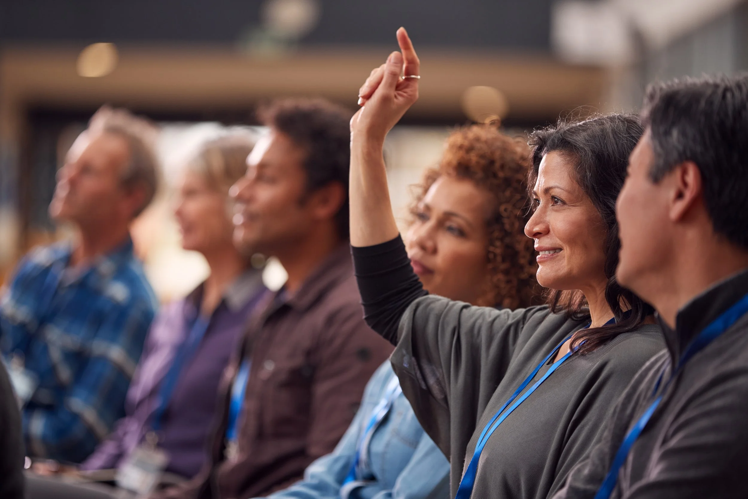 Personas en una conferencia o reunión, una mujer levanta la mano para hacer una pregunta o indicar algo.