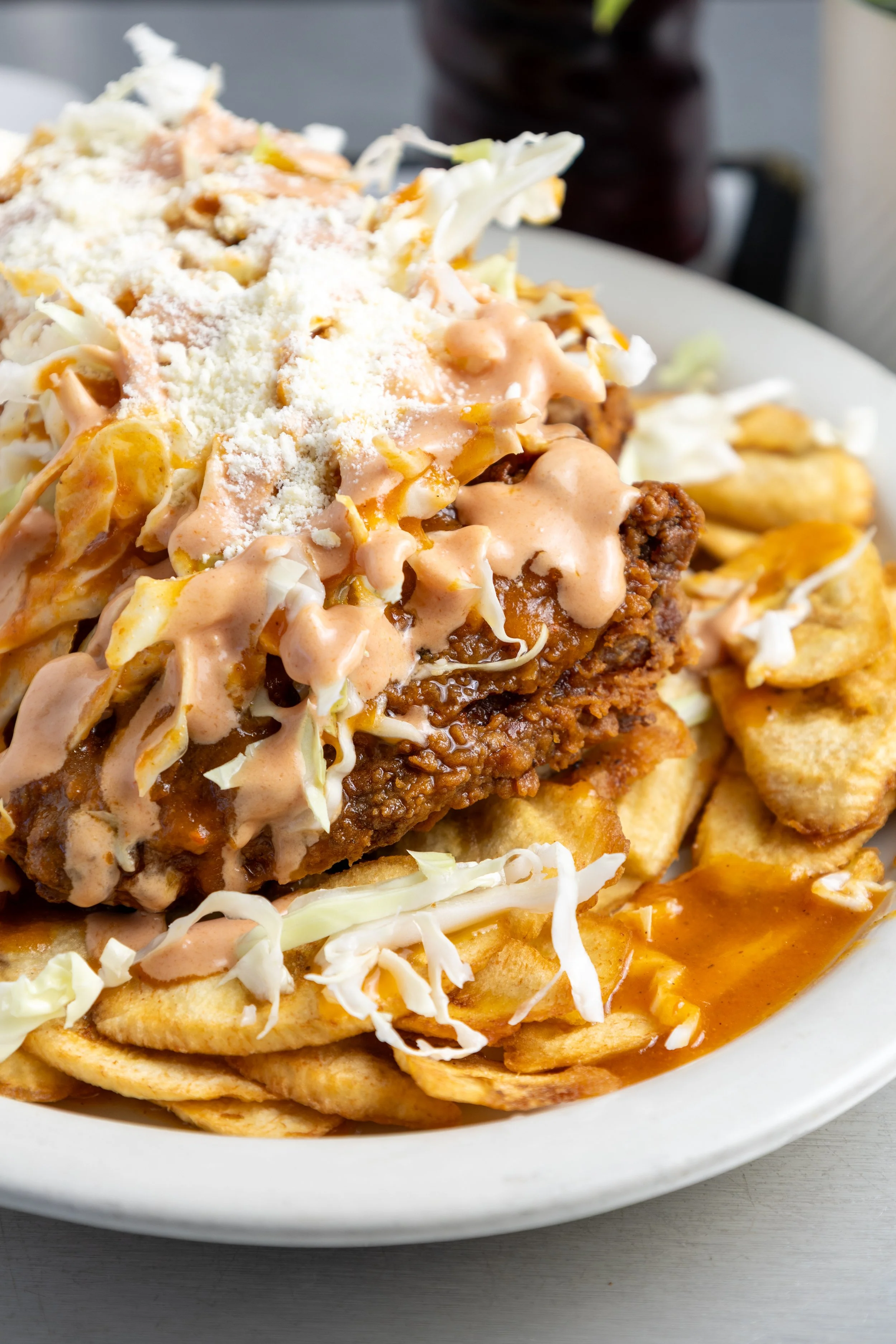 A plate of crispy fried chicken topped with shredded lettuce, drizzled with creamy sauce, shredded cheese, and serving of French fries on the side.