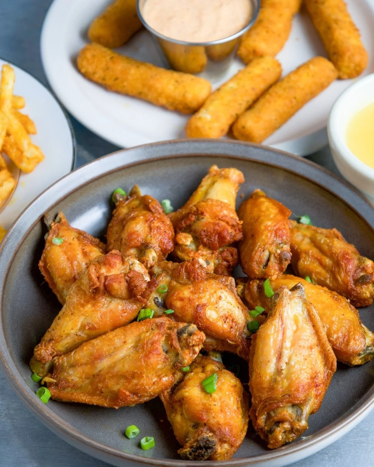 A black bowl filled with cooked chicken wings garnished with chopped green onions.