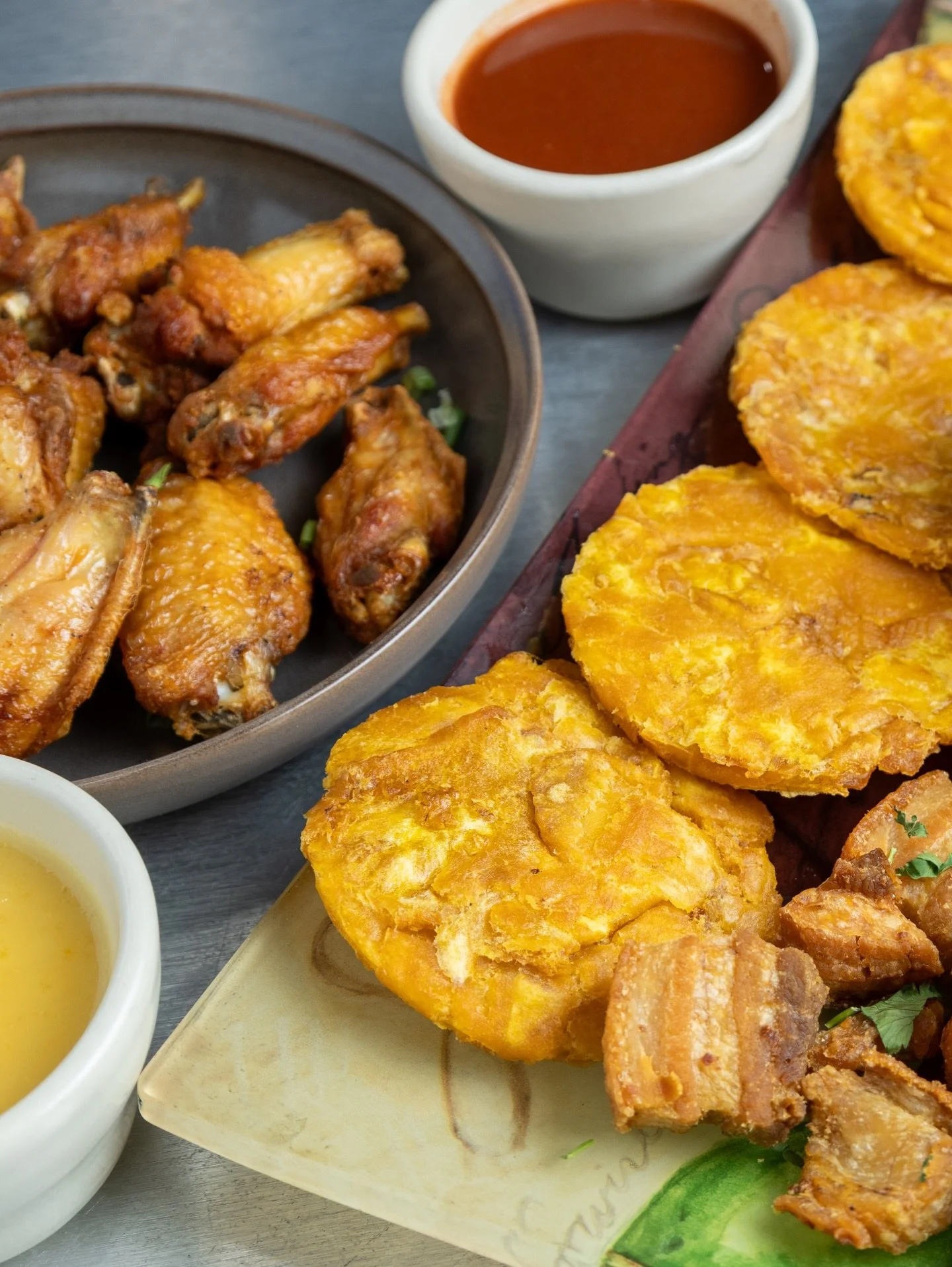 Fried chicken wings, fried plantains, dipping sauces, and a bowl of barbecue sauce on a table.