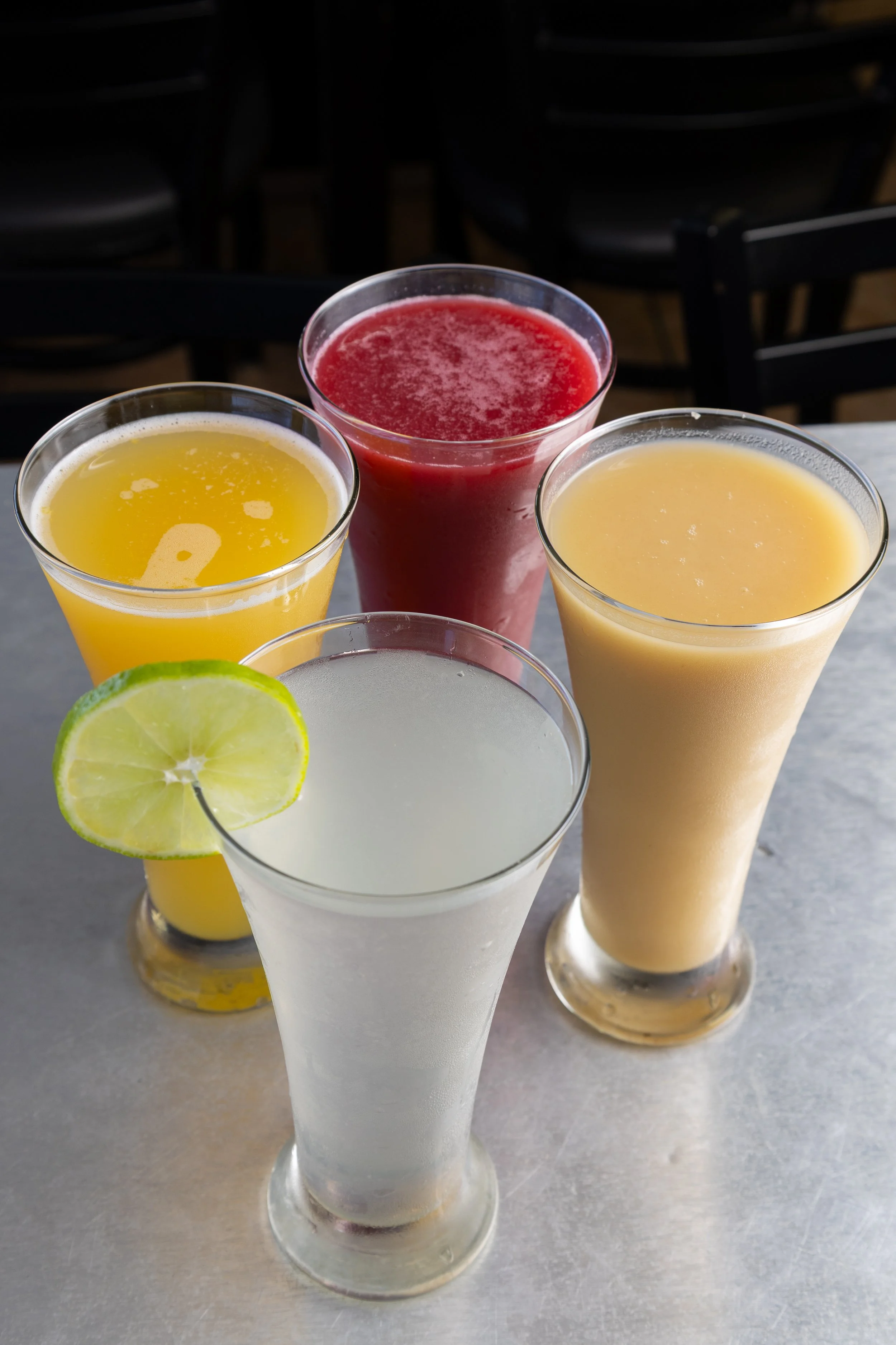Four tall glasses of colorful fruit drinks on a table, including a glass with a lemon slice garnish.