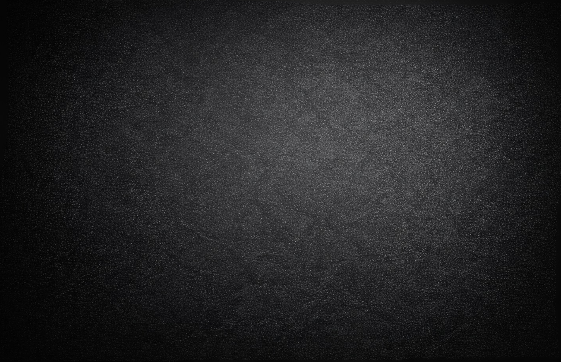 A dark textured surface, possibly metal or asphalt, with a grainy appearance.