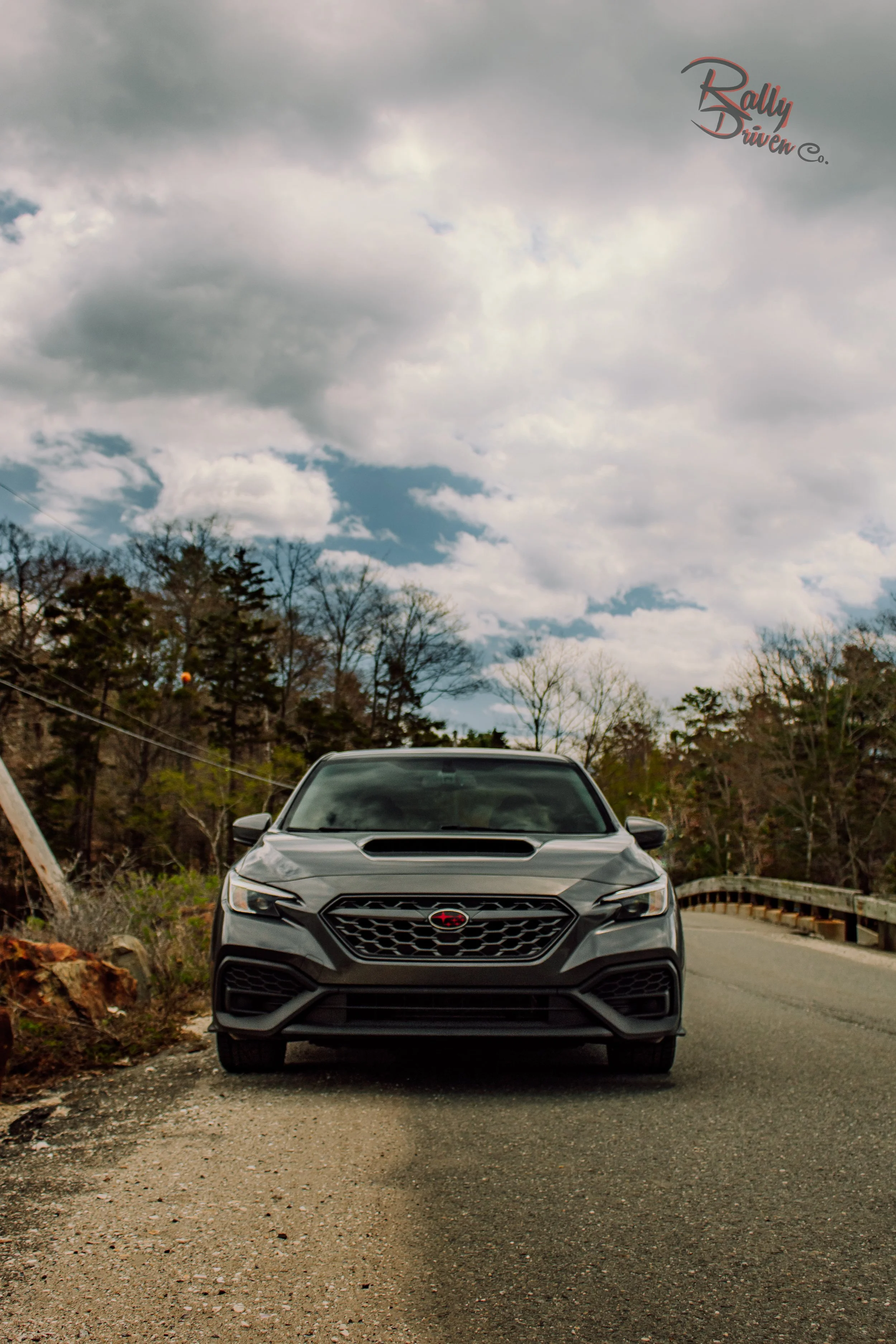 Gray SUV parked on a gravel road with a cloudy sky and trees in the background.