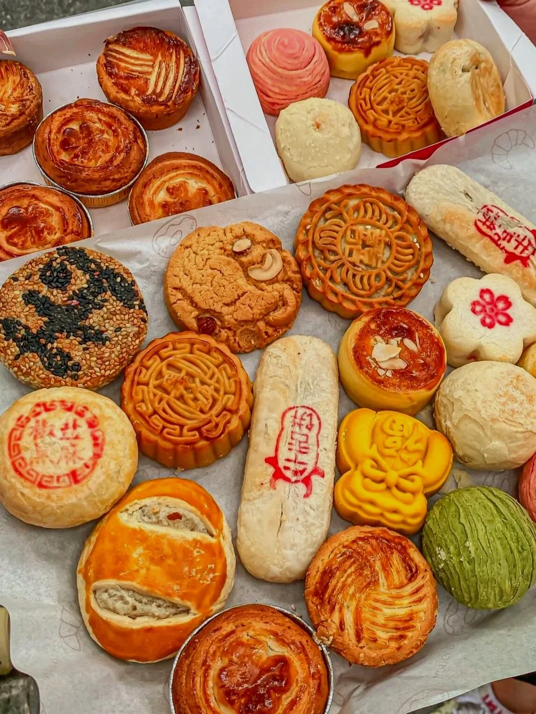 Assorted Chinese bakery pastries including mooncakes, egg tarts, and sesame seed cookies.