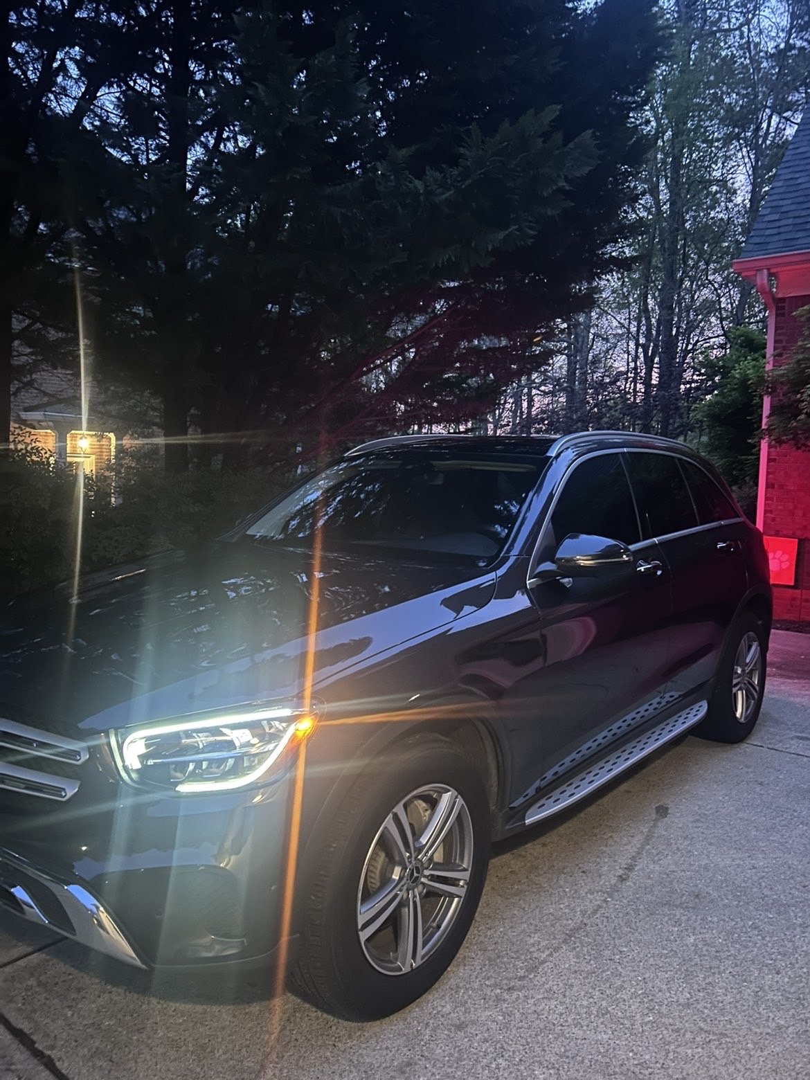 Black luxury SUV parked in a driveway during dusk, with trees and a red brick house visible in the background.