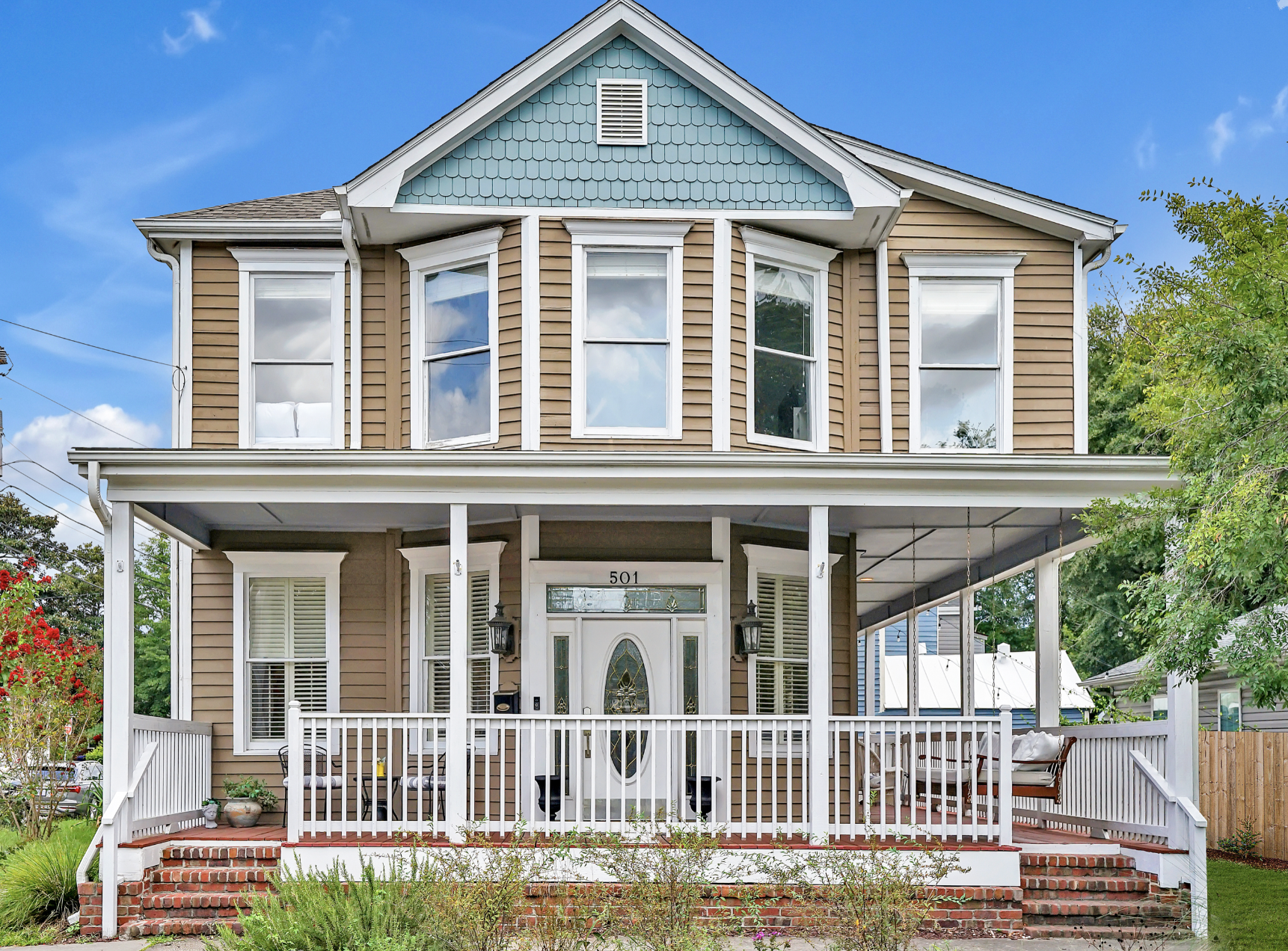 Two-story Victorian-style house in Wilmington, NC, with tan lap siding, a teal gabled upper facade, and a wide covered front porch. You can rent it for a wedding-related event like a wedding weekend, bachelorette party, bridal shower, baby shower, et