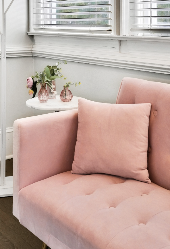 Close-up of a blush pink tufted velvet sofa with a matching throw pillow in a rentable Wilmington, NC event home, styled with pink glass bud vases and fresh florals on a marble side table — perfect for wedding weekends, bridal showers, bachelorette p
