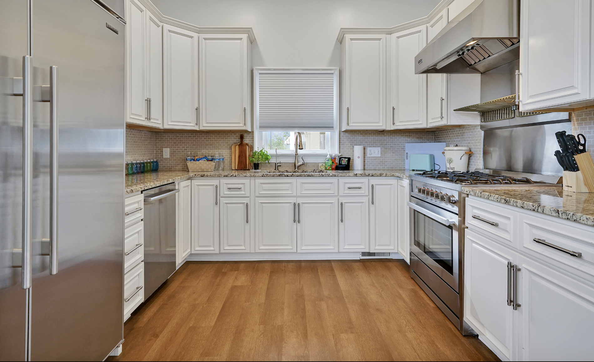 Spacious, fully equipped kitchen in a rentable Wilmington, NC event home, featuring white shaker cabinets, granite countertops, a gray subway tile backsplash, stainless steel appliances including a professional gas range and French door refrigerator,
