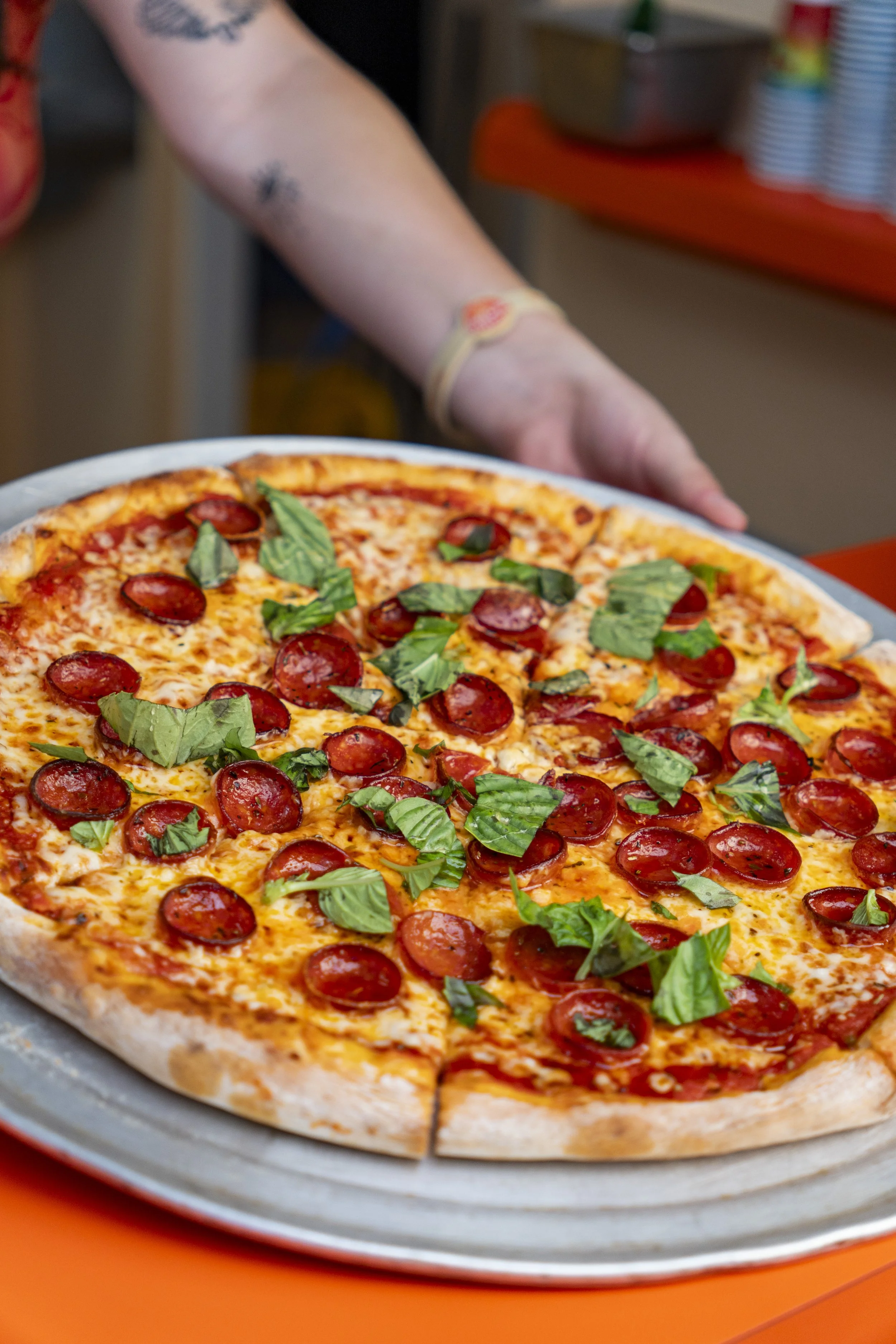 A freshly baked pepperoni pizza topped with fresh basil leaves, on a round metal tray.