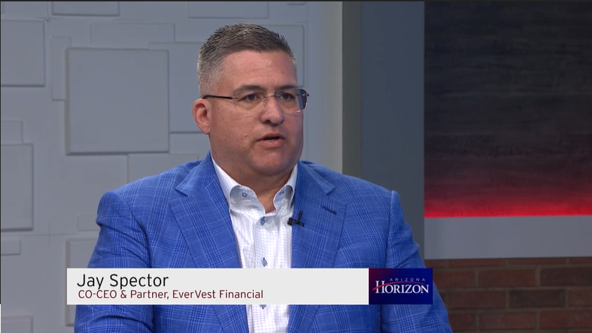 Jay Spector, co-CEO and partner of EverVest Financial, interviewed in a studio with a light-colored wall and a gray brick wall background, wearing a blue checkered blazer and glasses.