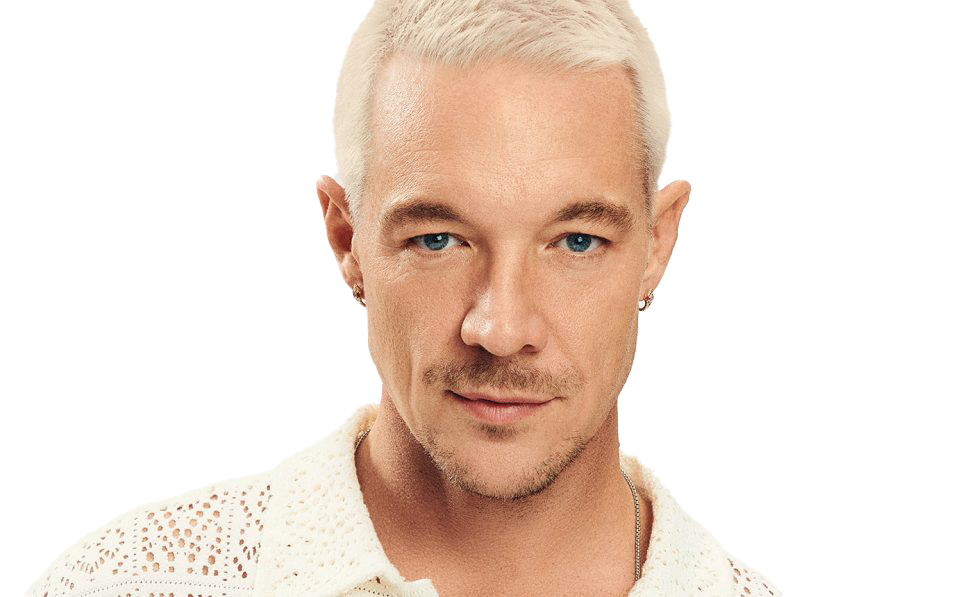 Close-up of a man with platinum blonde hair and blue eyes, wearing a white lacy top, smiling subtly.