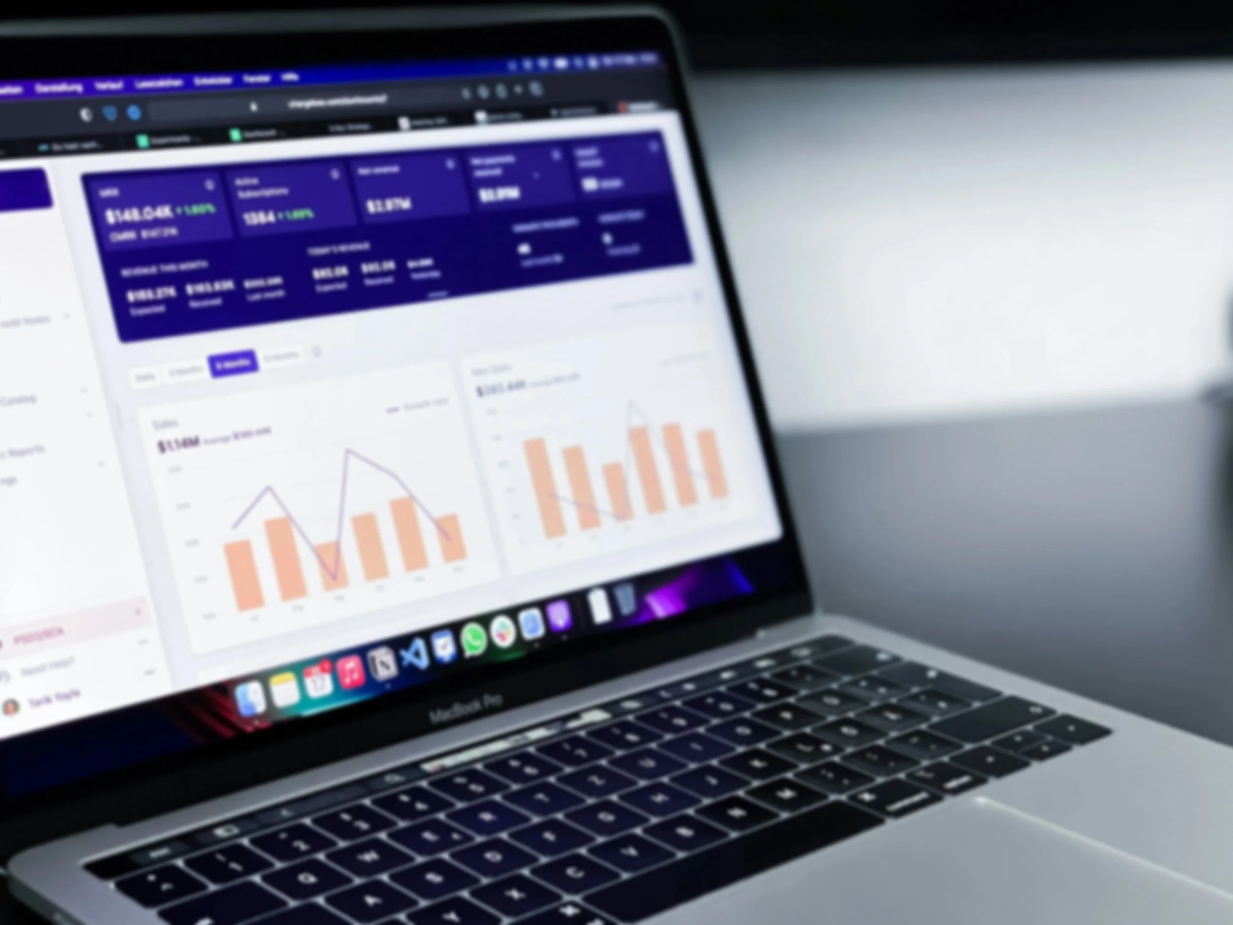 A MacBook Pro laptop displaying financial charts and graphs on a screen with a dark blue background, showing bar and line charts in peach and purple colors.